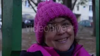 an Attractive Middle Aged Woman Smiles While Sitting on a Green Wooden Swing on a Park Playground