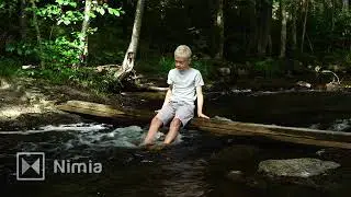 barefoot boy sitting on plank over river with feets in water