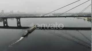 Barge laden with sand floating on empty calm river through loaded bridge in industrial downtown ...
