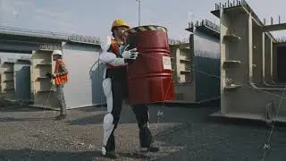 Male contractor in exoskeleton carrying barrel near supervisor