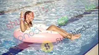 cute young girl is having fun in a swimming pool in sunny day, drifting on a pink inflatable ring, s