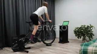 Indoor Virtual Cycling, Fit cycling woman rides bicycle at home on stationary bike out of saddle...