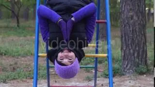 a Smiling Young Woman Hangs on Knees Being on a Playground Ladder and Doing Yoga Exercise in Autumn
