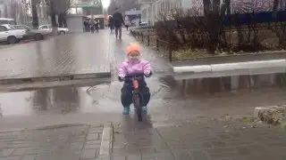 Дитя едет по луже на беговеле