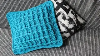 A crocheted pillow made of knitted yarn with a waffle pattern.