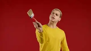 Creative man artist imitates painting with brush on red background  Fantasy, idea, non standard appr
