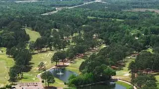 Aerial view of a vast golf course surrounded by lush green trees and water bodies on a sunny day in