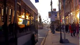 At sunset on sidewalk walking people, on a busy road drive cars and buses