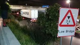 Truck and trailer crashed into low overhead bridge  and is stuck. It is freed by recovery truck