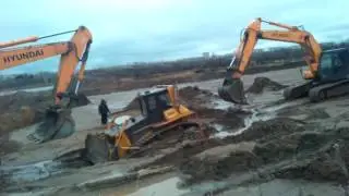 Вытаскивают бульдозер двумя эксковаторами зарюханого в песок.