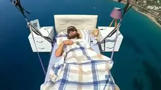 Man on bed suspended by parachutes flies away and takes a nap