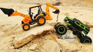 Excavator tractor pulls a monster truck toy car out of the mud. The truck was in an accident