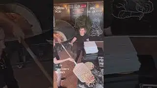Two pizza restaurant employees have trouble picking up the pizza and getting it into the o