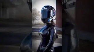 GIRL IN A BLACK GLITTERED LEATHER COSTUME AND A MOTORCYCLE HELMET ON A MOTORCYCLE.