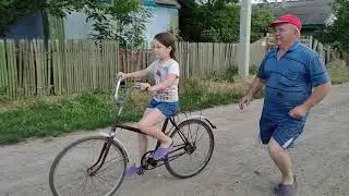 Дедушка учит Лизку кататься на велосипеде.