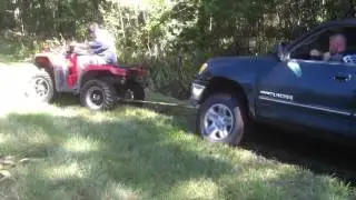 Four wheeler pulling out truck in deep mud hole